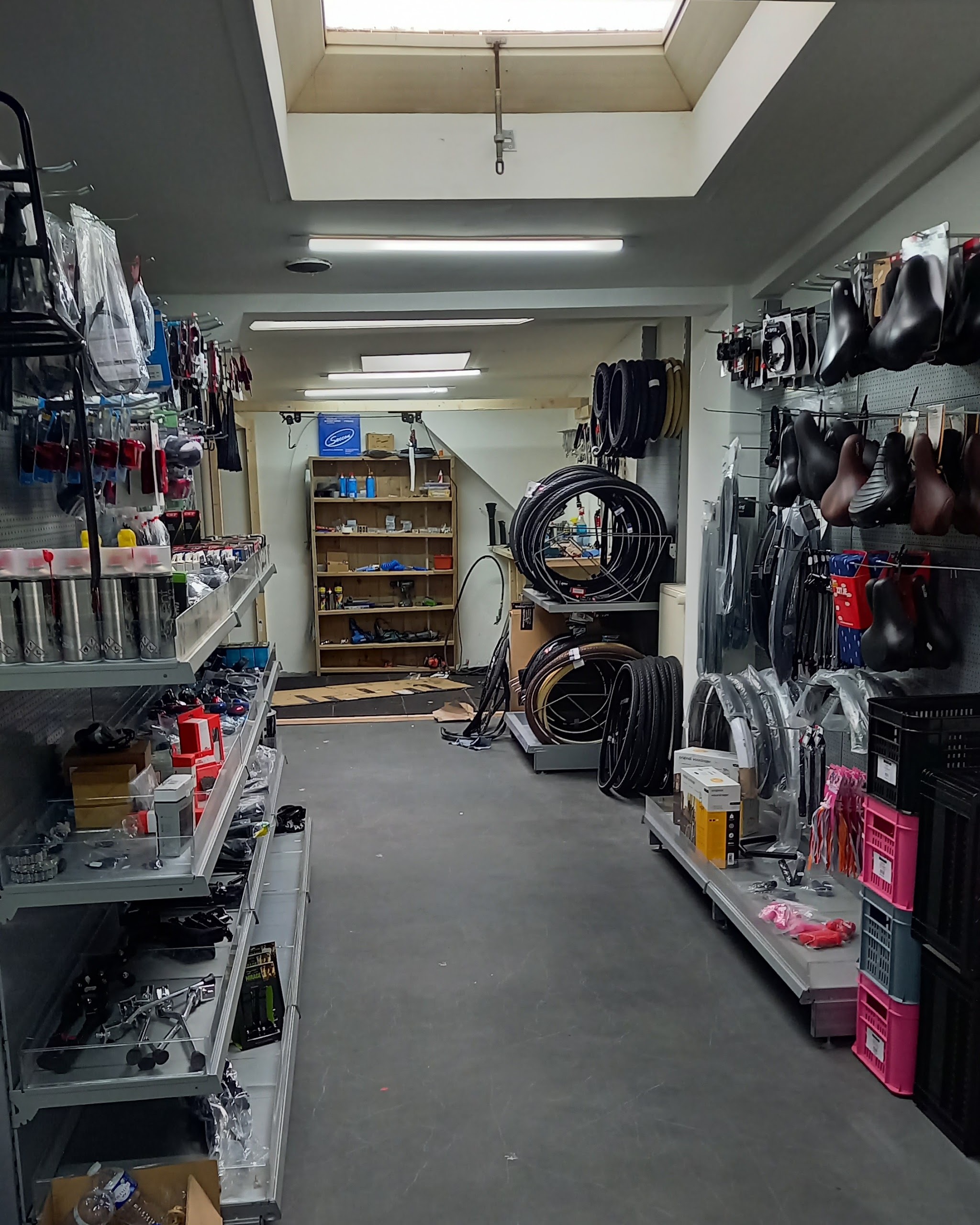 De onderdelenwand in de winkel: zadels, banden, kabels en kratten, met de werkplaats achterin