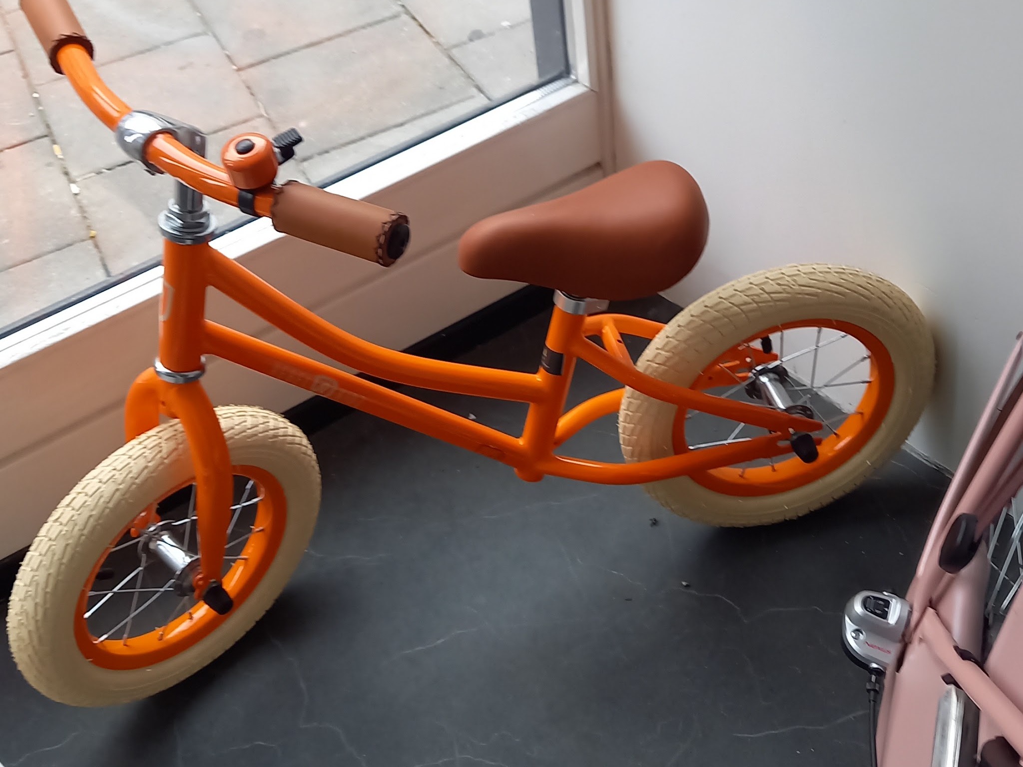 Oranje loopfiets met crèmekleurige banden bij het raam